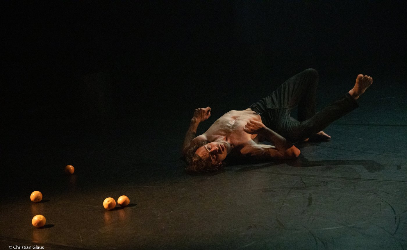 Dominik Wagner lying on stage among scattered oranges in WAY OUT
